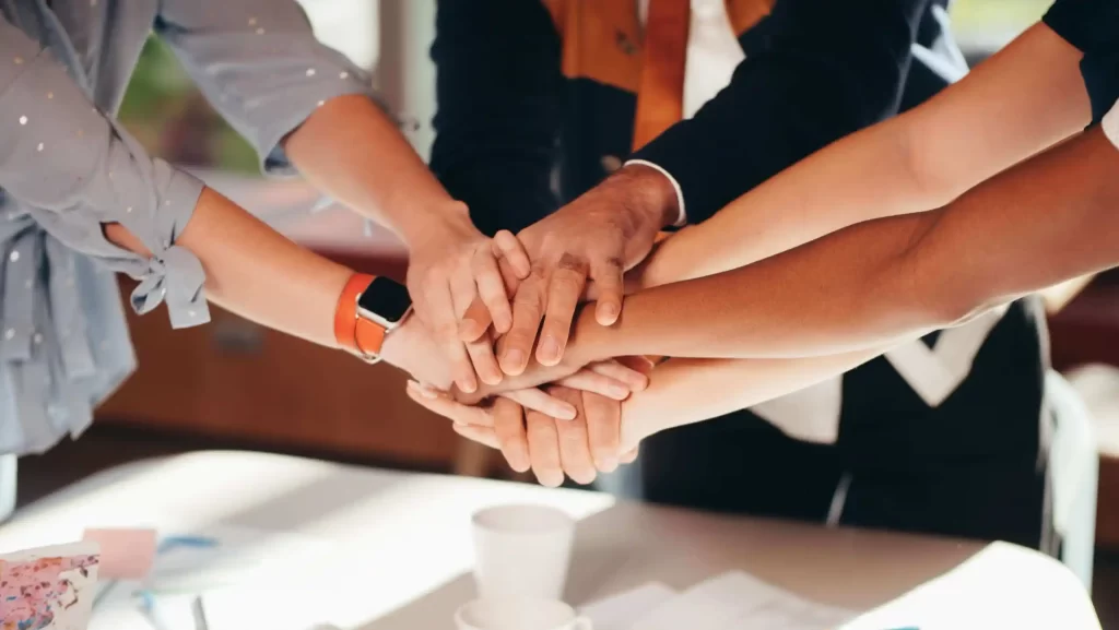 The Next Resourcing team demonstrates unity by placing their hands on top of one another, symbolizing collaboration and teamwork in recruiting resourcing services